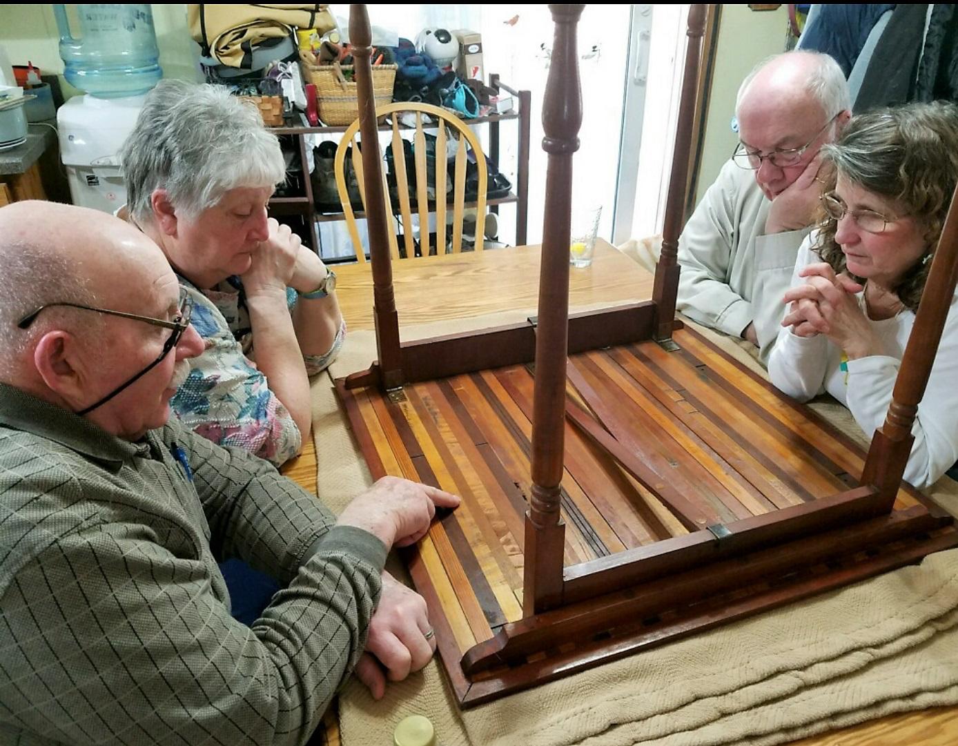 This photo shows on left, Bonnie and Dick Lancaster, and on right George and Tracy Riedesel examining the bottom of the mystery table on April 1, 2018. Photo by Val Macer